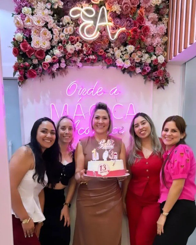 Dra. Eliana Andrade com a equipe em frente ao neon "Onde a mágica acontece"
